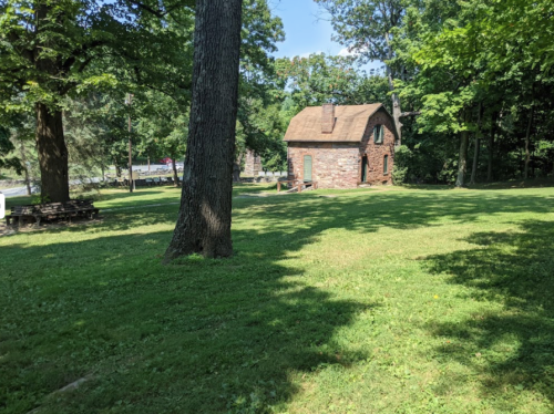 A small stone house surrounded by lush green trees and grass on a sunny day.