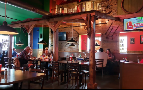 A cozy restaurant interior with wooden decor, tables, and patrons enjoying meals under warm lighting.