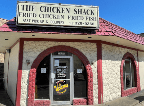 Exterior of The Chicken Shack, featuring a sign for fried chicken and fish, with a welcoming entrance and open hours posted.