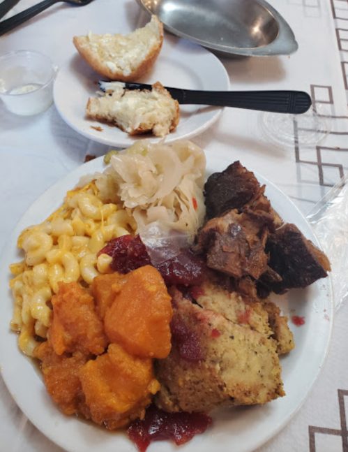 A plate of food with macaroni and cheese, sweet potatoes, stuffing, sauerkraut, and a piece of cornbread.