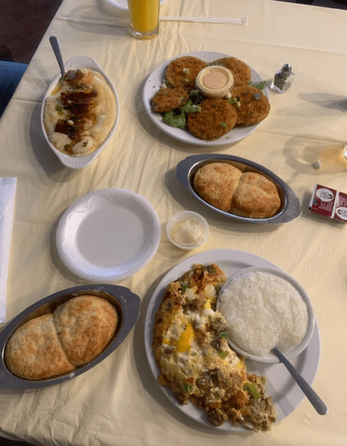 A table with various dishes: fried patties, grits, biscuits, and a plate of scrambled eggs with vegetables.