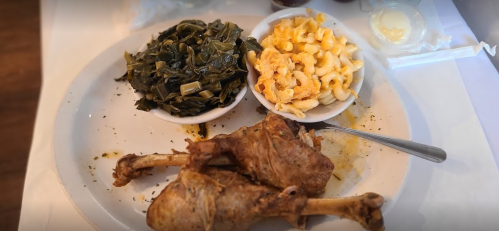 A plate with two chicken drumsticks, collard greens, and macaroni and cheese served in bowls.