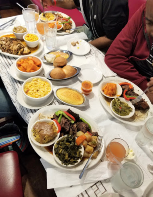 A table filled with various dishes, including meats, vegetables, macaroni, and desserts, with drinks in clear glasses.