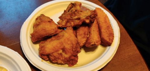 A plate of crispy fried chicken pieces and sweet potato fries on a white paper plate.