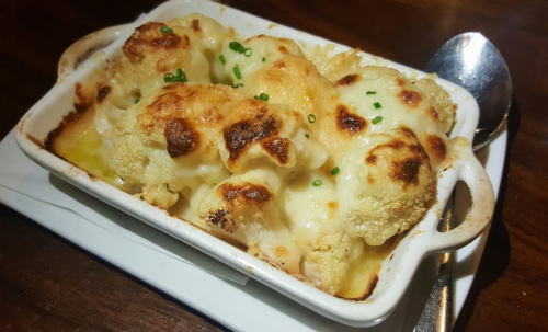 Baked cauliflower in a creamy cheese sauce, topped with green onions, served in a small white dish.