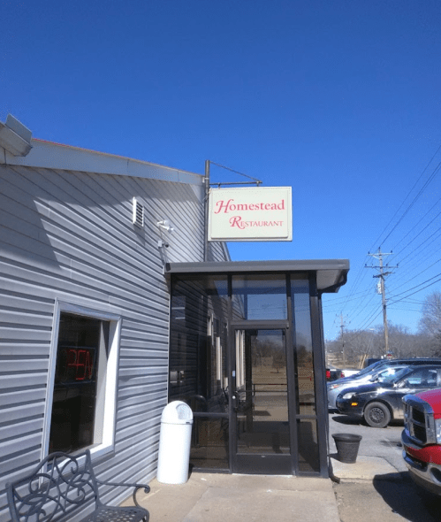 Exterior of Homestead Restaurant with a clear blue sky, featuring an "OPEN" sign and parked cars nearby.