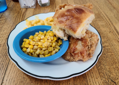 A plate with fried chicken, two biscuits, and a side of corn and macaroni and cheese.