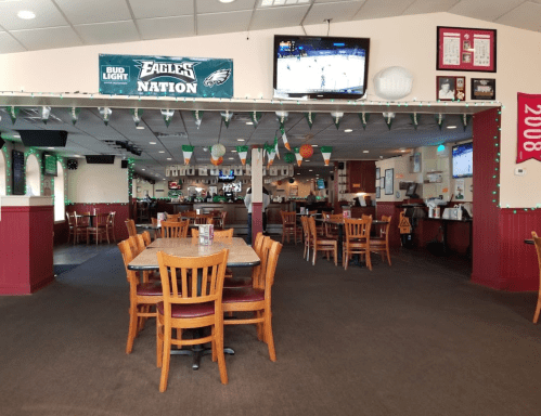 A spacious restaurant interior with wooden tables and chairs, decorated for a sports event, featuring TVs and festive lights.