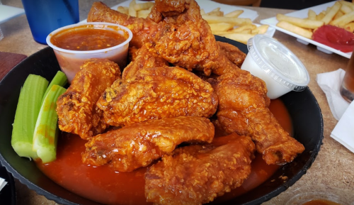 A plate of crispy chicken wings coated in sauce, served with celery sticks and dipping sauces, alongside fries.