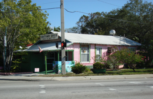 A pink house with a sign reading "Chattaway Drive-In" surrounded by greenery, located at a street corner.