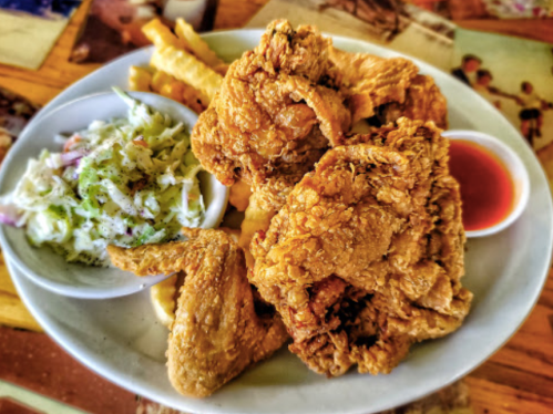A plate of crispy fried chicken with coleslaw, fries, and a small bowl of dipping sauce.