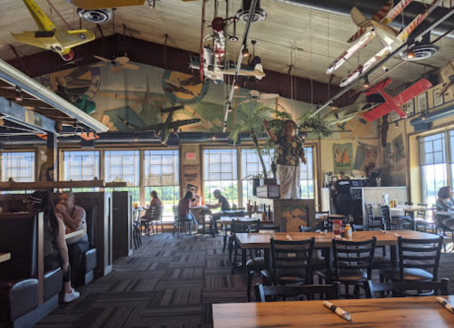 A cozy restaurant interior with airplane decor, booths, and diners enjoying their meals. Bright and inviting atmosphere.