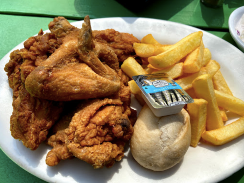 A plate of fried chicken, French fries, a biscuit, and a small container of butter on a green table.