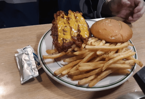 A plate with a cheeseburger, crispy fries, and a packet of condiments on a wooden table.