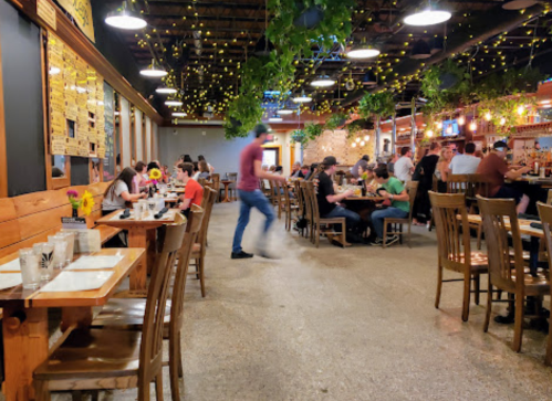 A lively restaurant interior with wooden tables, string lights, and patrons enjoying their meals.