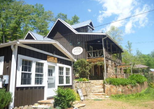 A rustic two-story building with a stone foundation, surrounded by trees and a clear blue sky.