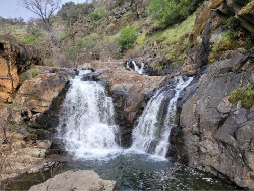 A serene waterfall cascading over rocky terrain, surrounded by lush greenery and rugged hills.