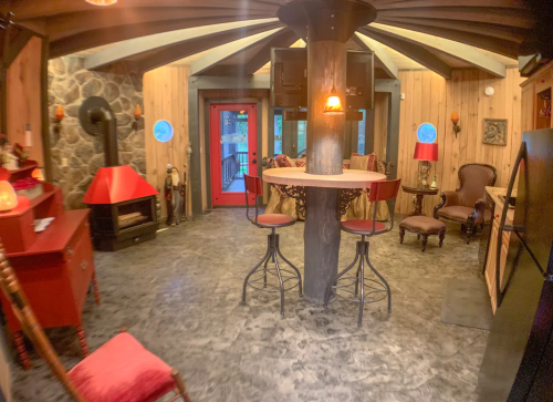 Cozy interior of a rustic cabin with wooden walls, a round bar, and a stone fireplace, featuring warm lighting.