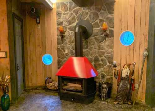 Cozy room featuring a red wood stove, stone wall, decorative statues, and blue circular windows.