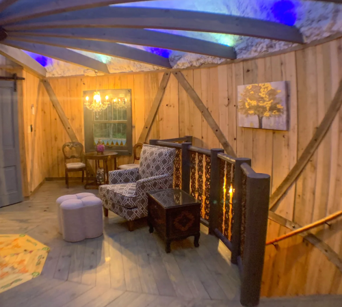 Cozy interior with wooden walls, a patterned chair, a small table, and decorative lighting under a curved ceiling.