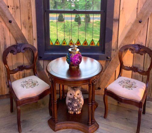 A cozy corner with two ornate chairs, a small table, and a decorative owl, framed by a stained glass window.