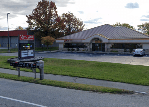 A restaurant building with a gold roof and sign, surrounded by grass and trees, with a few parked cars outside.