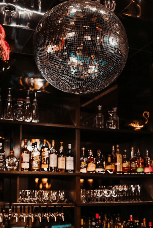 A sparkling disco ball hangs above a well-stocked bar with various bottles and glassware on display.
