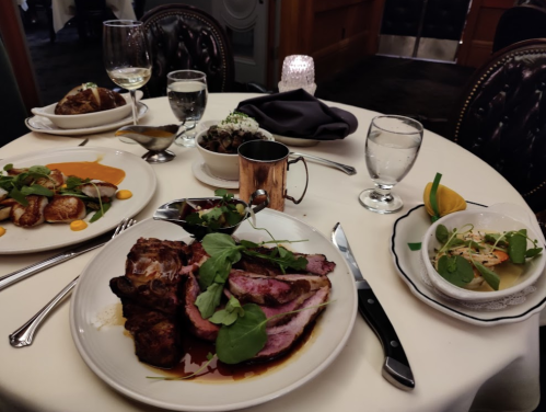 A beautifully set table with gourmet dishes, including roast meat, seafood, and sides, alongside drinks and elegant tableware.