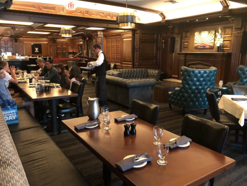 A cozy restaurant interior with wooden decor, tables set for dining, and a waiter serving guests.