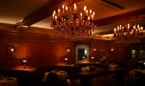 Elegant restaurant interior with dim lighting, featuring ornate chandeliers and rich wooden paneling.
