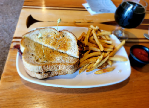 A toasted sandwich with two toothpicks, served with a side of fries and a small bowl of ketchup on a wooden table.