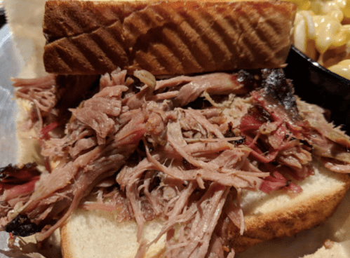 Close-up of a pulled pork sandwich with tender meat on soft bread, served alongside macaroni and cheese.
