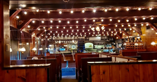 Cozy restaurant interior with wooden decor, warm lighting, and a bar area in the background.