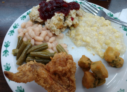 A plate of food featuring fried chicken, green beans, white beans, corn, stuffing with cranberry, and fried okra.