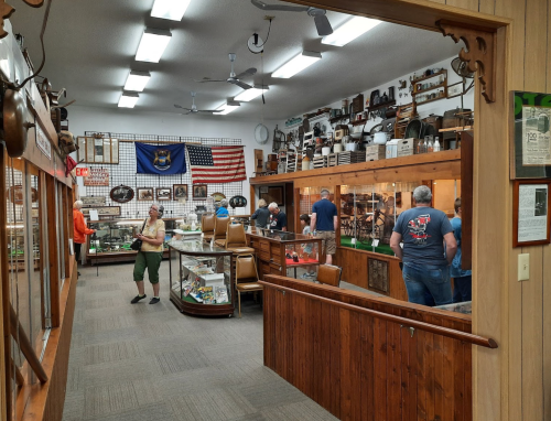 A museum interior with displays, visitors exploring exhibits, and walls adorned with historical items and flags.