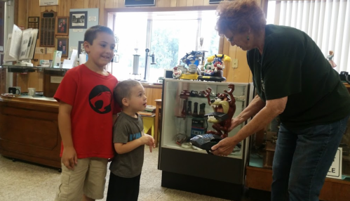 Two children watch as a woman shows them a decorative item in a museum setting.