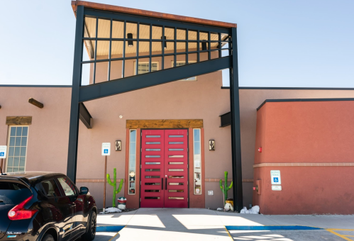 Modern building entrance with a striking red door, large windows, and cacti flanking the walkway.