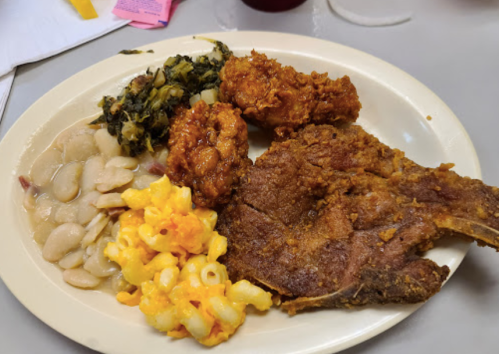A plate of food featuring fried chicken, pork chop, macaroni and cheese, greens, and beans.