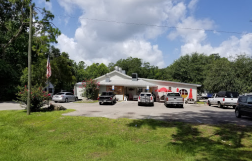 A small building with a red and white exterior, surrounded by trees, with several parked cars in front.