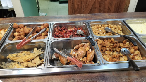 A buffet display featuring various fried seafood, including fish, shrimp, and crab, with sides and utensils for serving.