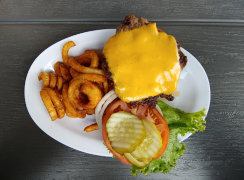 A cheeseburger with melted cheese, lettuce, tomato, pickles, and curly fries on a white plate.