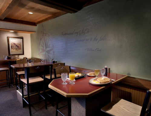 A cozy dining area with a table set for breakfast, featuring pancakes, juice, and a decorative wall with a quote.