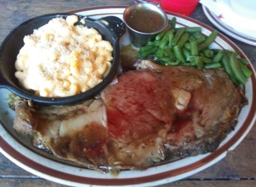 A plate featuring a juicy prime rib, green beans, and a side of macaroni and cheese in a small skillet.