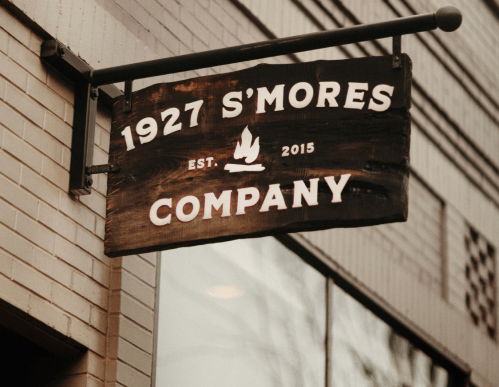 Sign for "1927 S'mores Company," established in 2015, featuring a campfire graphic.