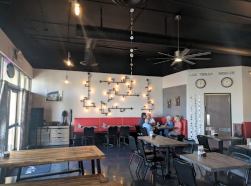 Interior of a modern restaurant featuring red booths, wooden tables, and decorative lighting. Customers are dining together.