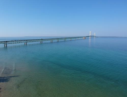 A long bridge spans over calm blue waters under a clear blue sky.