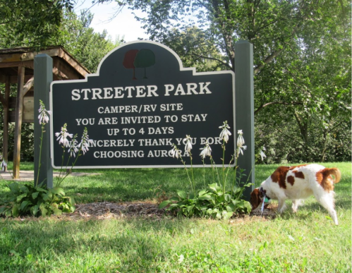 A sign for Streeter Park welcomes campers and RVs, with a dog sniffing the grass nearby.