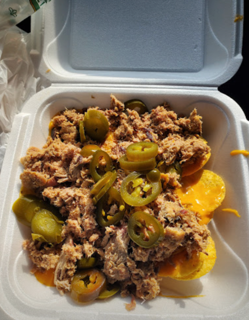 A takeout container filled with shredded meat, jalapeños, and cheese over tortilla chips.