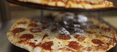 A close-up of a pepperoni pizza on a rack, with another pizza above it, both freshly baked and steaming.