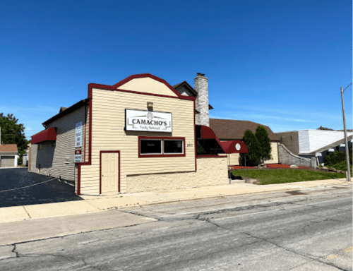 A two-story building with a sign reading "Camacho's Family Restaurant," featuring a red awning and clear blue sky.